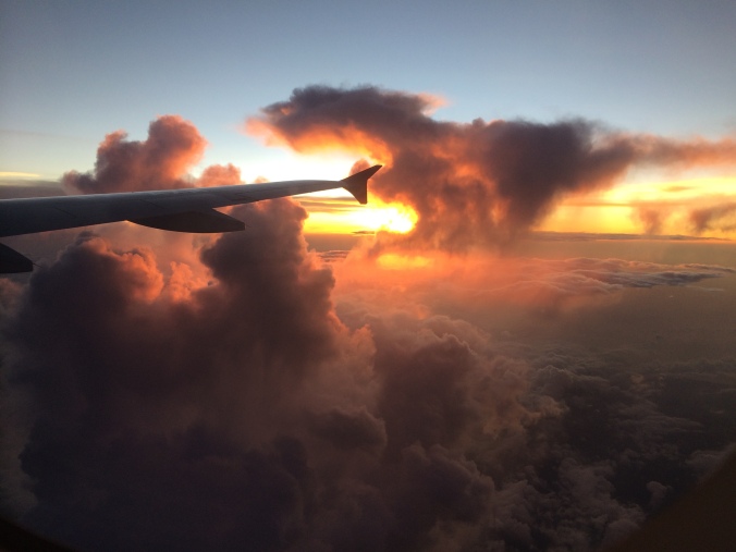 A plane wing with clouds and a sunset out an airplane window