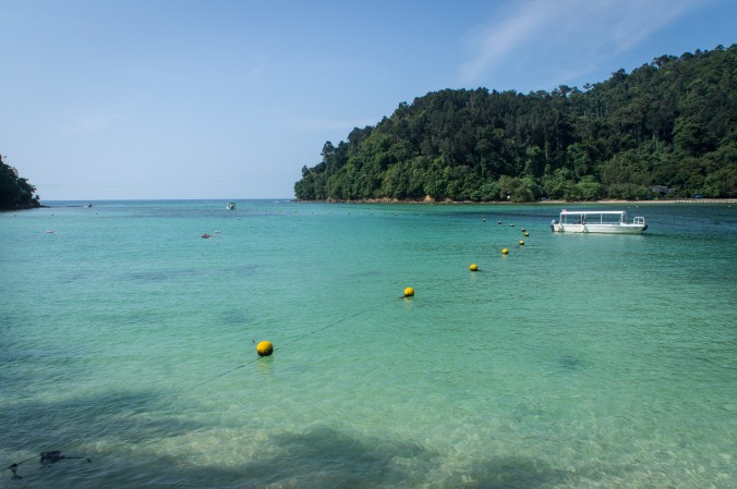 View of the water, a boat, and Gaya Island from the shore of Sapi Island, Malaysia